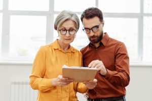 Zwei Personen im Büro studieren gemeinsam ein Dokument auf einem Clipboard, konzentriert auf die Inhalte.